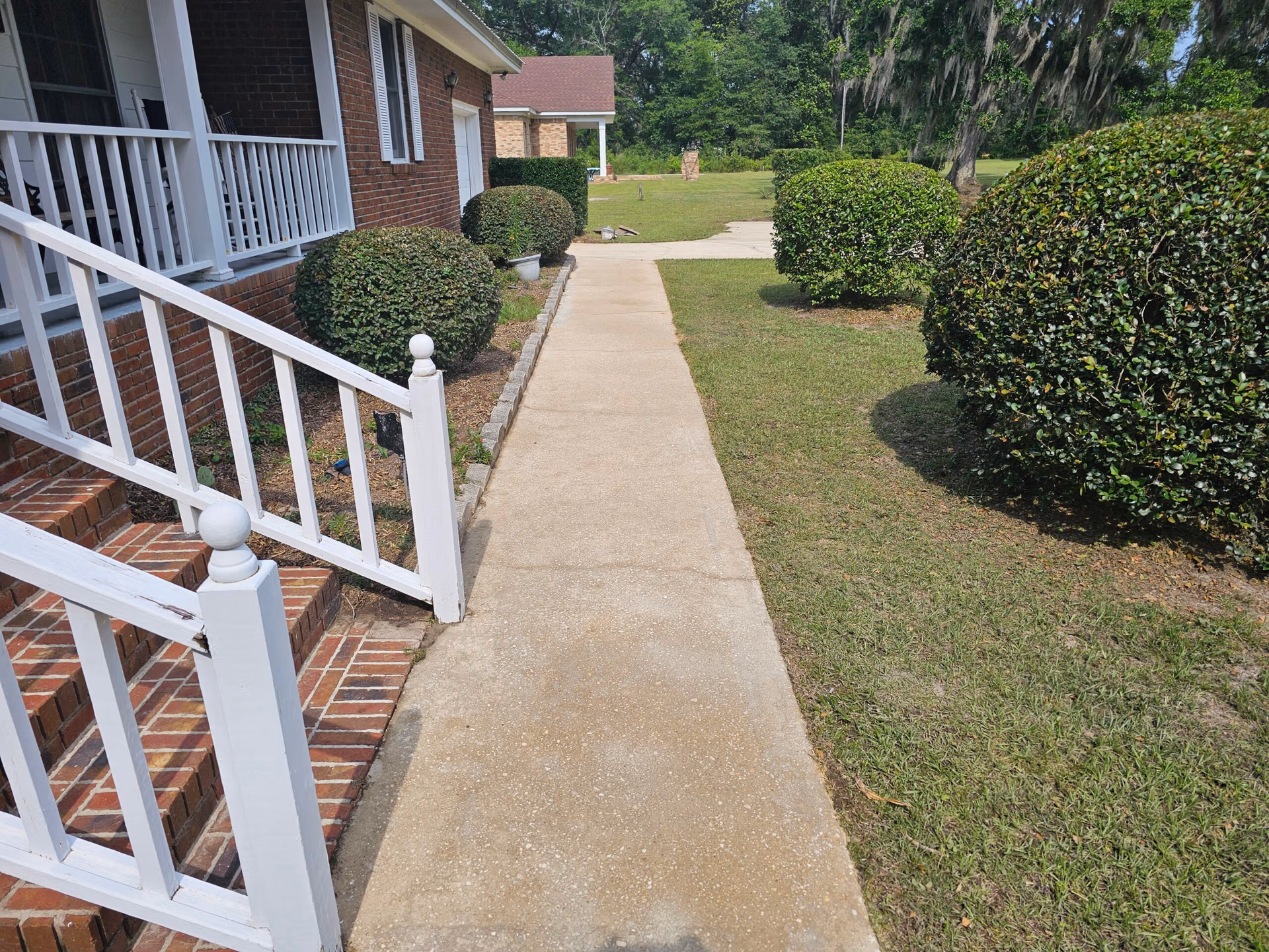 Pressure washed concrete walkway leading to a residential front porch with white railing.