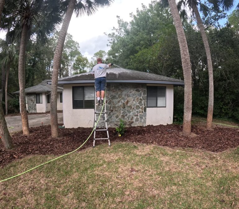 Roof Cleaning 3 Soft washing the roof edge of a stone-front home from a ladder in Tallahassee, FL
